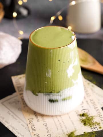 Green liver detox smoothie made with herbal liver greens layered over creamy plant milk in a ribbed glass, styled on a slate board with wellness powders and a wooden spoon.