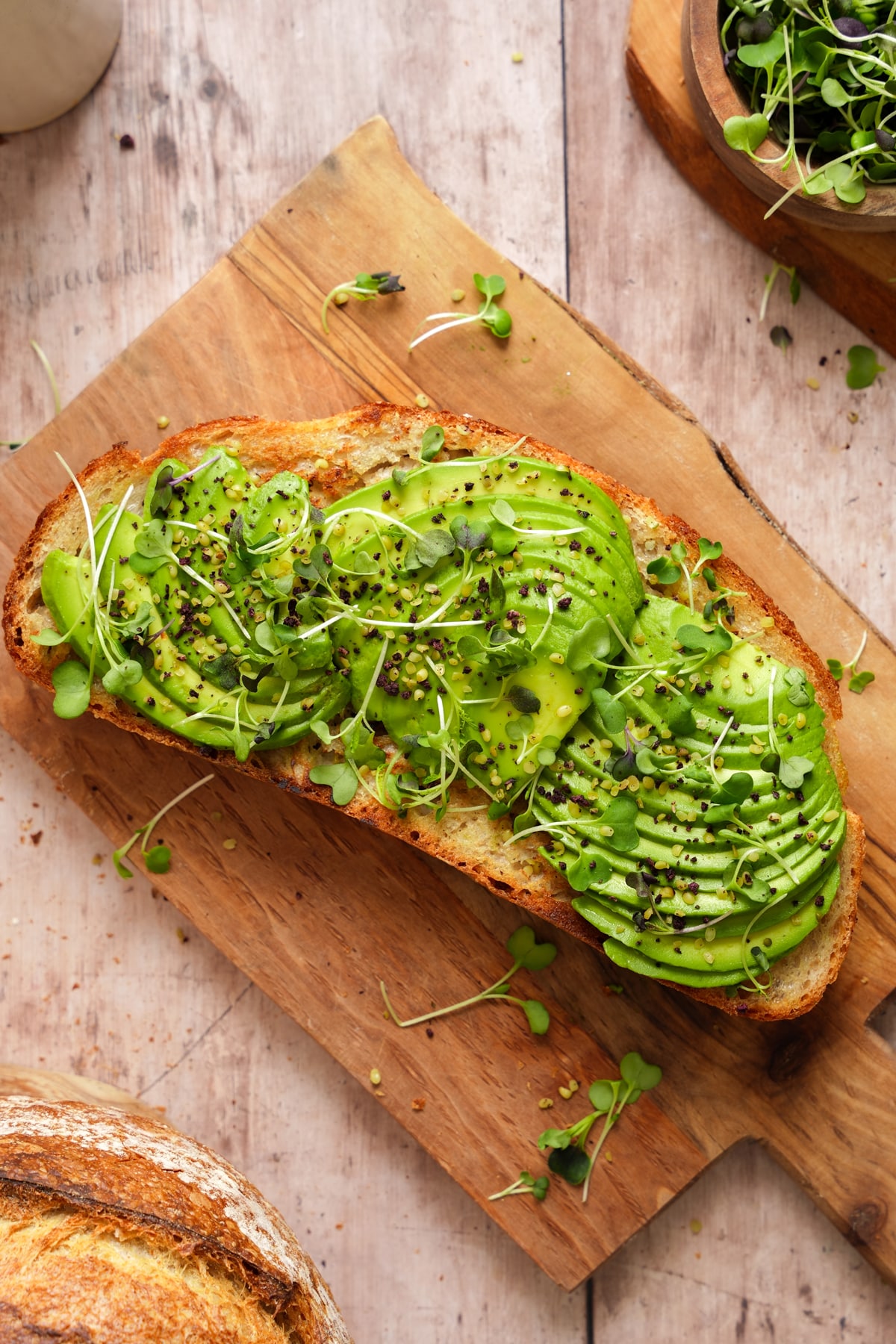Golden toasted bread topped with neatly sliced avocado, microgreens, and a sprinkle of seasoning, served on a wooden board.