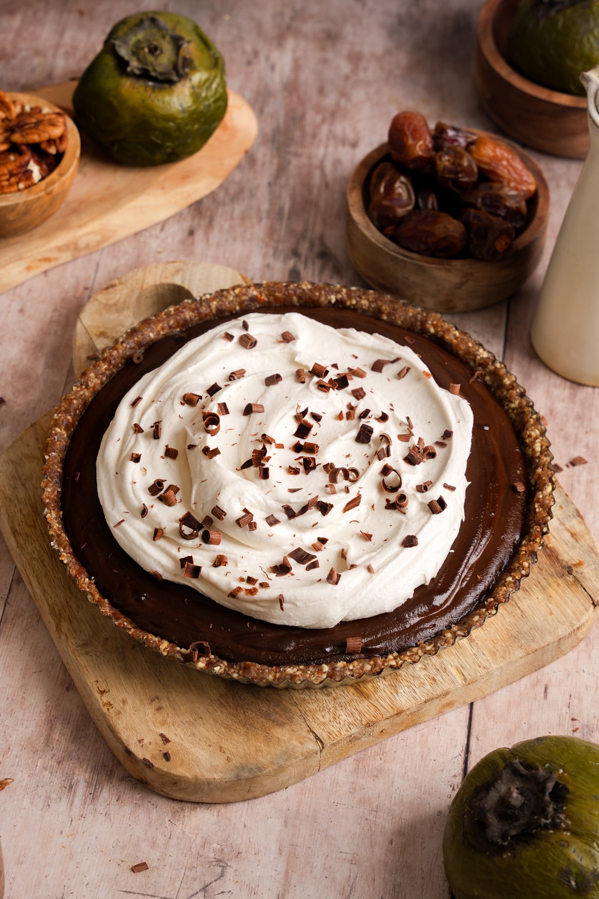 Vegan black sapote pie with chocolate filling and whipped topping in a nut-based crust, garnished with chocolate shavings and surrounded by fresh black sapote and dates