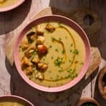 Creamy vegan potato soup topped with crispy croutons, fresh chives, and a drizzle of olive oil in a rustic bowl