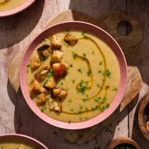 Creamy vegan potato soup topped with crispy croutons, fresh chives, and a drizzle of olive oil in a rustic bowl