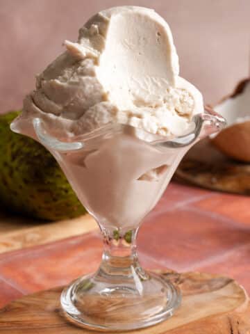 Close-up of creamy vegan soursop ice cream in a glass dessert dish with a smooth texture and tropical ingredients in the background