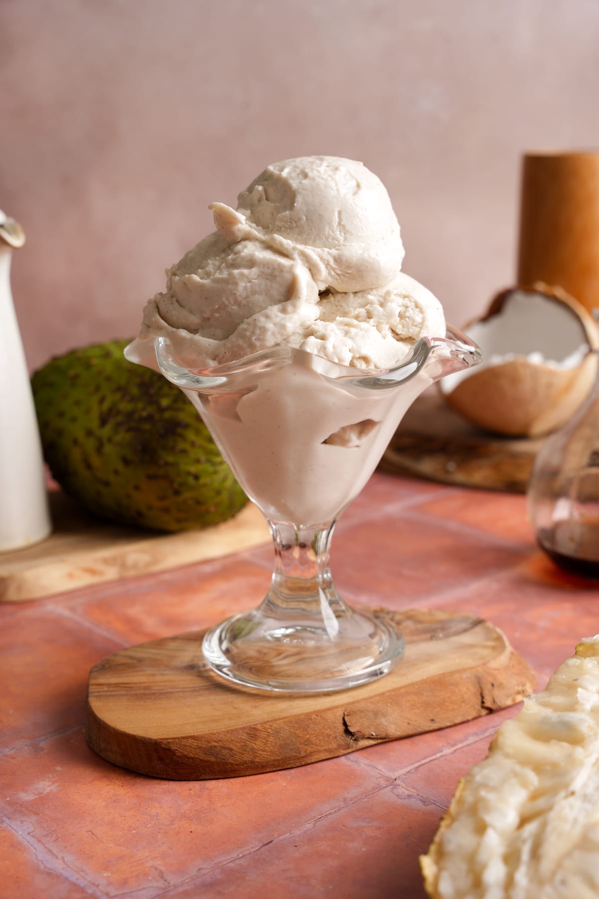 Creamy vegan soursop ice cream scooped into a glass dessert dish with fresh soursop and coconut in the background