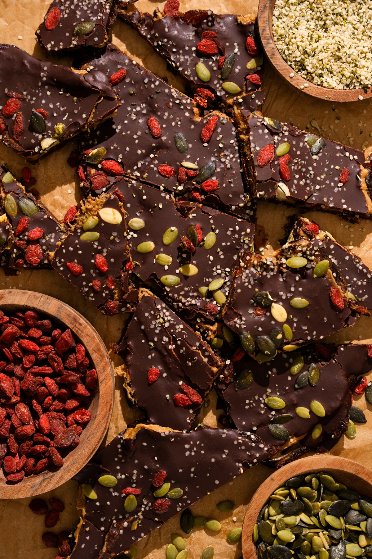 Healthy superfood date bark topped with dark chocolate, goji berries, pumpkin seeds, and hemp seeds on parchment paper