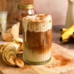 Healthy iced vegan banana latte topped with fluffy banana cold foam and a sprinkle of cinnamon. This creamy dairy-free coffee drink is layered with espresso and plant-based milk, served with fresh banana slices for an easy homemade café-style beverage.