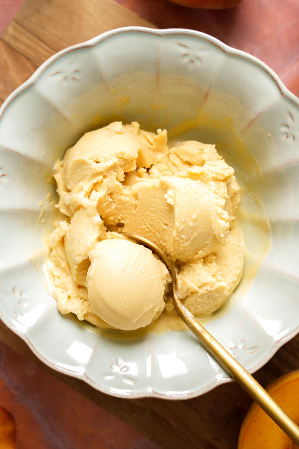 Creamy homemade vegan peach ice cream served in a light blue ceramic bowl with a gold spoon. This dairy-free peach ice cream is smooth, rich, and made with simple ingredients, making it the perfect refreshing summer dessert.