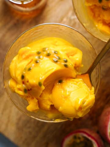 A close-up of creamy homemade passion fruit sorbet topped with fresh passion fruit pulp in a glass dessert bowl. This easy vegan passion fruit sorbet is naturally dairy-free, gluten-free, refined sugar-free, and bursting with bright tropical flavor.