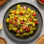 Close-up of homemade vegan pesto gnocchi coated in a vibrant basil pesto and served on a black plate. The dish is topped with juicy cherry tomatoes, toasted pine nuts, and shaved vegan Parmesan, creating a fresh, colorful, and comforting plant-based meal.