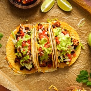 Overhead view of loaded vegan tofu tacos filled with seasoned tofu and black beans, shredded lettuce, pico de gallo, and creamy cilantro lime dressing, served with lime wedges and fresh cilantro.