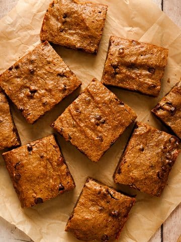 Overhead view of vegan SunButter chocolate chip cookie bars cut into squares and arranged on parchment paper, with golden-brown tops and visible chocolate chips.