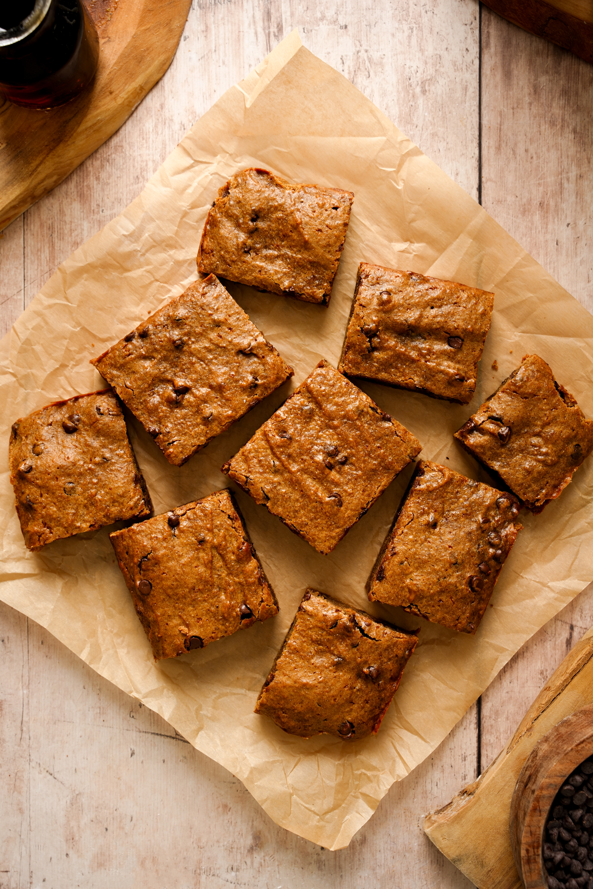 Overhead view of vegan SunButter chocolate chip cookie bars cut into squares and arranged on parchment paper, with golden-brown tops and visible chocolate chips.