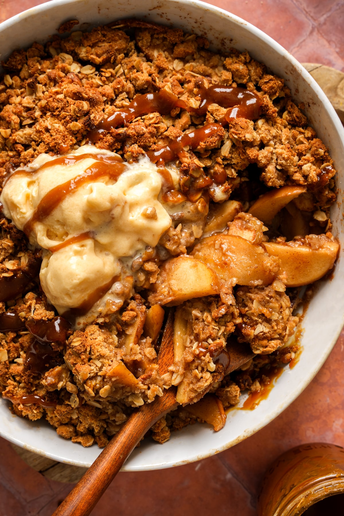 Close-up of healthy vegan apple crisp with tender cinnamon apples and a golden oat crumble, topped with vegan vanilla ice cream and a drizzle of caramel sauce.