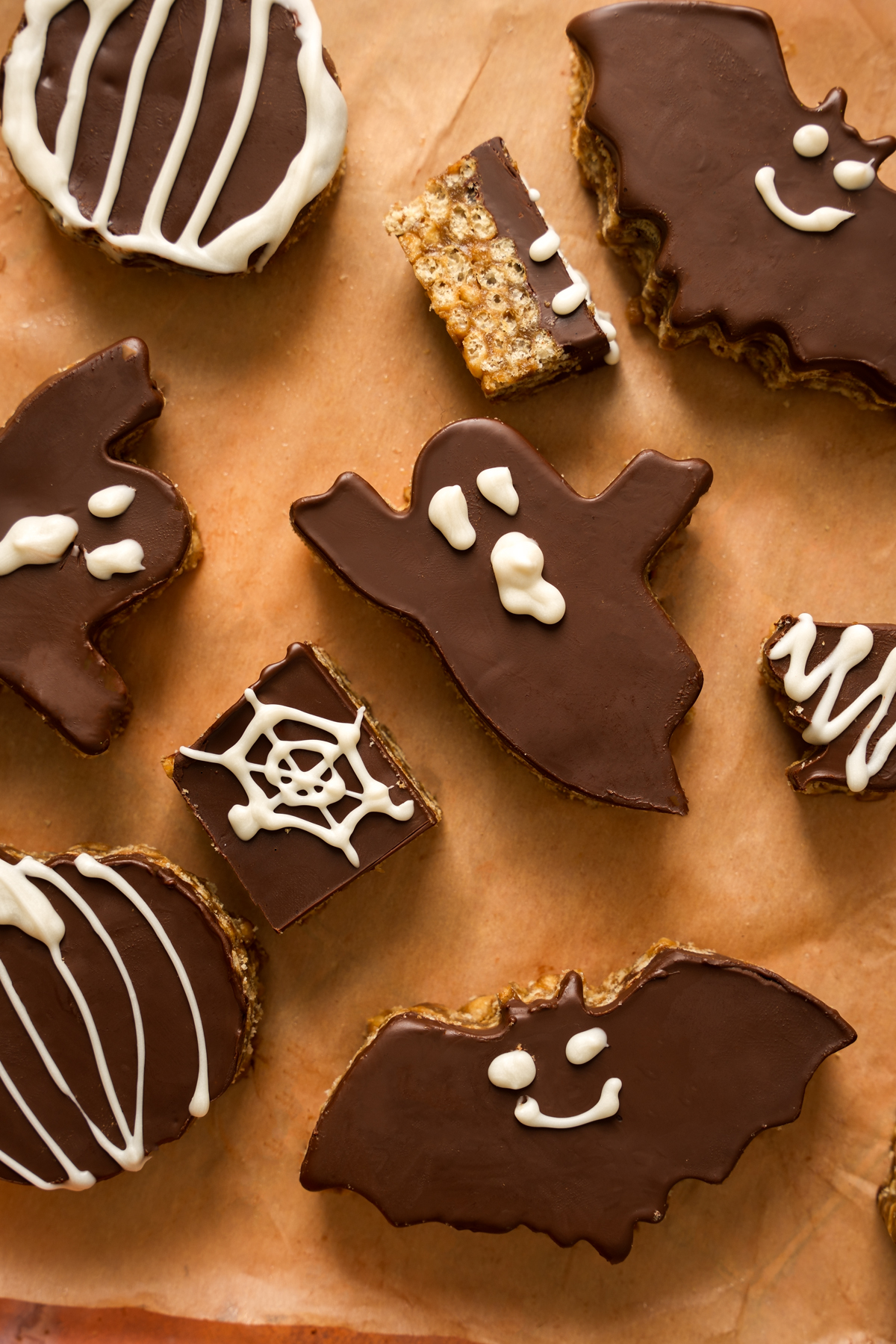 Close-up of a ghost-shaped SunButter Chocolate Halloween Bar with a smooth chocolate topping and white chocolate face, surrounded by bat-shaped bars and crispy rice squares on parchment paper.